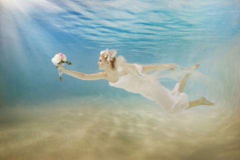 Caucasian bride in wedding dress swimming under water