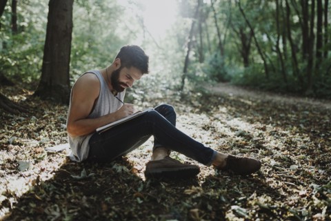 Caucasian man sitting in woods drawing on sketchpad