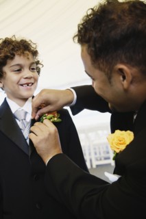 Hispanic father fastening boutonniere for son