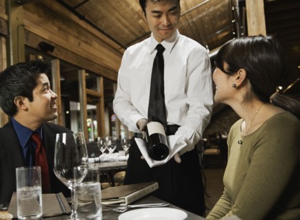 Asian waiter showing wine to couple