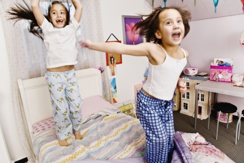 Asian sisters jumping on bed