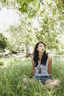 Asian woman sitting cross-legged in grass