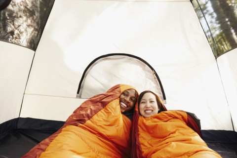 Multi-ethnic couple inside sleeping bags and tent