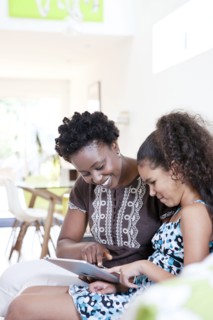 Mother and daughter using digital tablet in living room