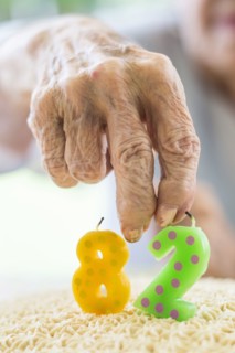 Close up of wrinkled hand holding birthday cake candle