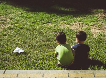 Hispanic brothers with paper airplane on lawn