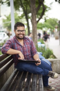 Smiling Hispanic man sitting on bench reading brochure