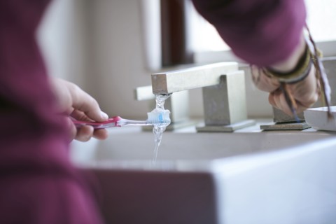 Hispanic man wetting toothbrush in sink