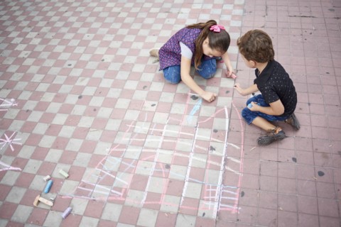 Hispanic boy and girl drawing with chalk on sidewalk