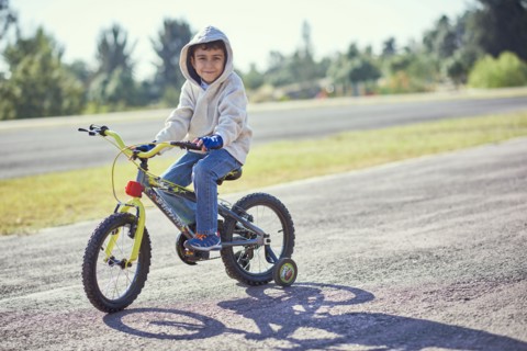 Hispanic boy posing on bicycle with training wheels