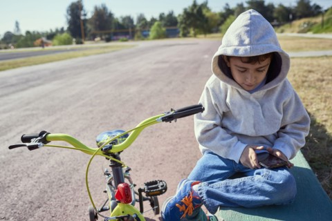 Hispanic boy sitting near bicycle texting on cell phone