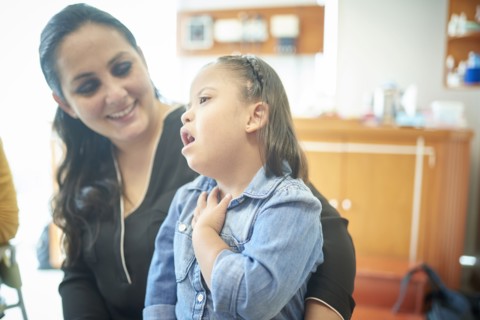 Hispanic mother watching daughter with Down Syndrome pointing to neck
