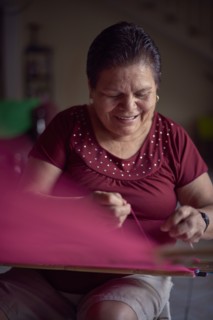 Hispanic woman weaving fabric on loom