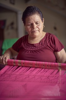 Hispanic woman weaving fabric on loom
