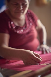Hispanic woman weaving fabric on loom