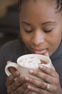 African woman smelling cup of hot cocoa with marshmallows