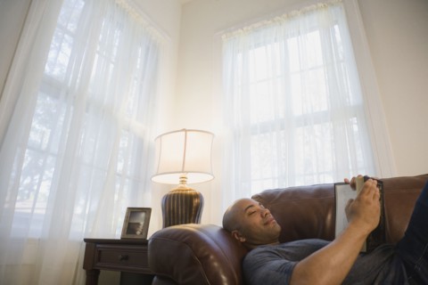 Mixed race man laying on sofa reading book