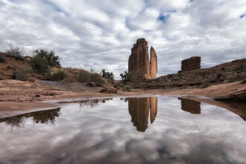 Reflection of rock formation and clouds in puddle