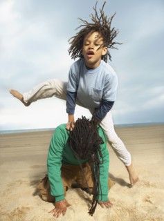 Mixed Race boy jumping over father on beach