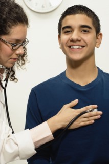 Female doctor checking young male patient with stethoscope