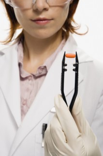 Female lab technician holding pill in large tweezers