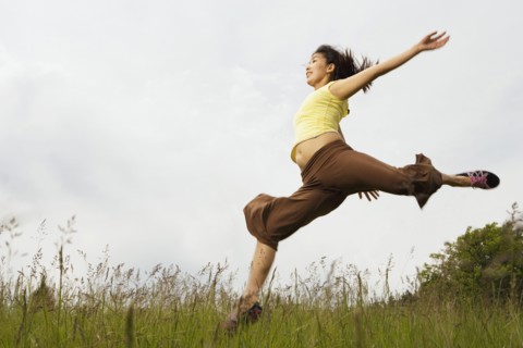 Asian woman jumping in meadow