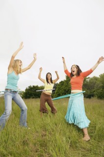Three young women playing with plastic hoops in meadow