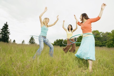 Three young women playing with plastic hoops in meadow
