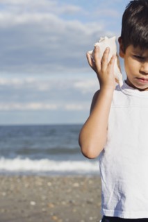 Young Hispanic boy listening to seashell