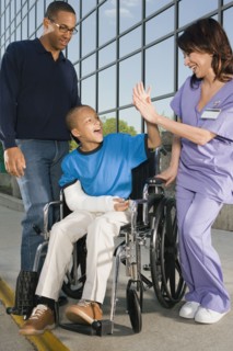 African boy in wheelchair high-fiving nurse in front of hospital