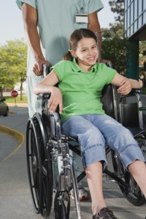Girl in wheelchair with nurse on sidewalk next to hospital