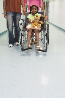African girl smiling in wheelchair with parents in hospital