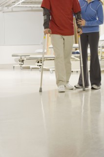 Woman helping man walk on crutches in hospital