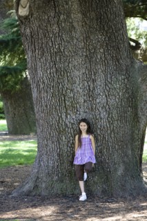 Mixed race girl leaning against tree trunk in park