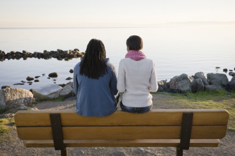 Black couple sitting on bench near shore