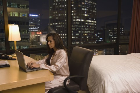 Hispanic woman typing on laptop in hotel room