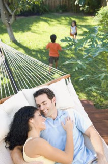 Couple relaxing in hammock with children playing in background