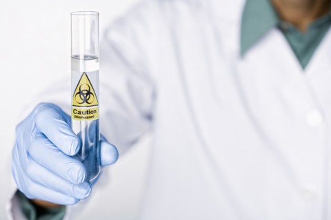 Hispanic scientist holding test tube with caution sticker full of water