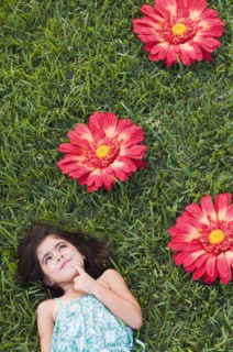 Mixed race girl laying in grass next to large flowers