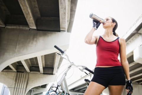Hispanic woman with bicycle drinking water