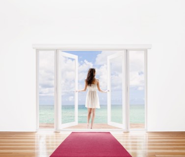 Hispanic woman opening French doors to ocean view
