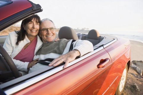 Older couple driving convertible on beach