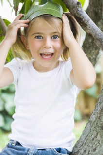 Caucasian girl sitting in tree holding leaf in hair