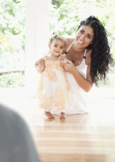 Mixed Race mother kneeling on floor helping baby daughter walking
