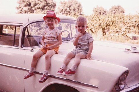 Caucasian brother and sister sitting on vintage car