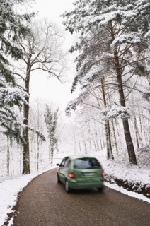 Green car driving on narrow road in winter