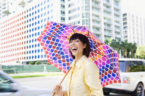 Laughing Mixed Race woman carrying umbrella in city