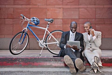 Business people sitting on curb using digital tablet and cell phone