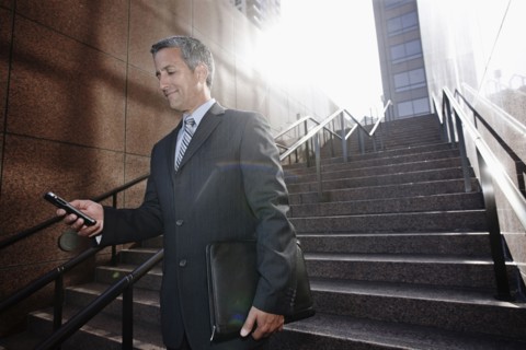 Hispanic businessman text messaging on steps