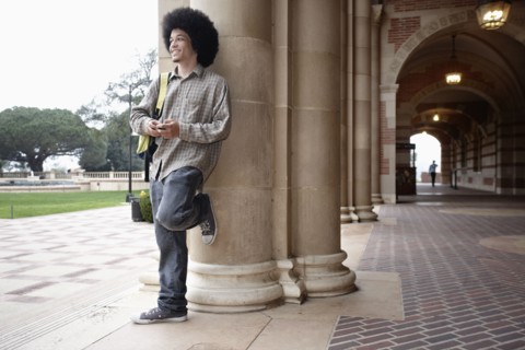 Student with afro leaning against pillar on campus
